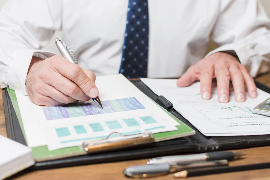 Close-up of a businessman reviewing financial tax charts and data, holding a pen and analysing printed reports on a desk.